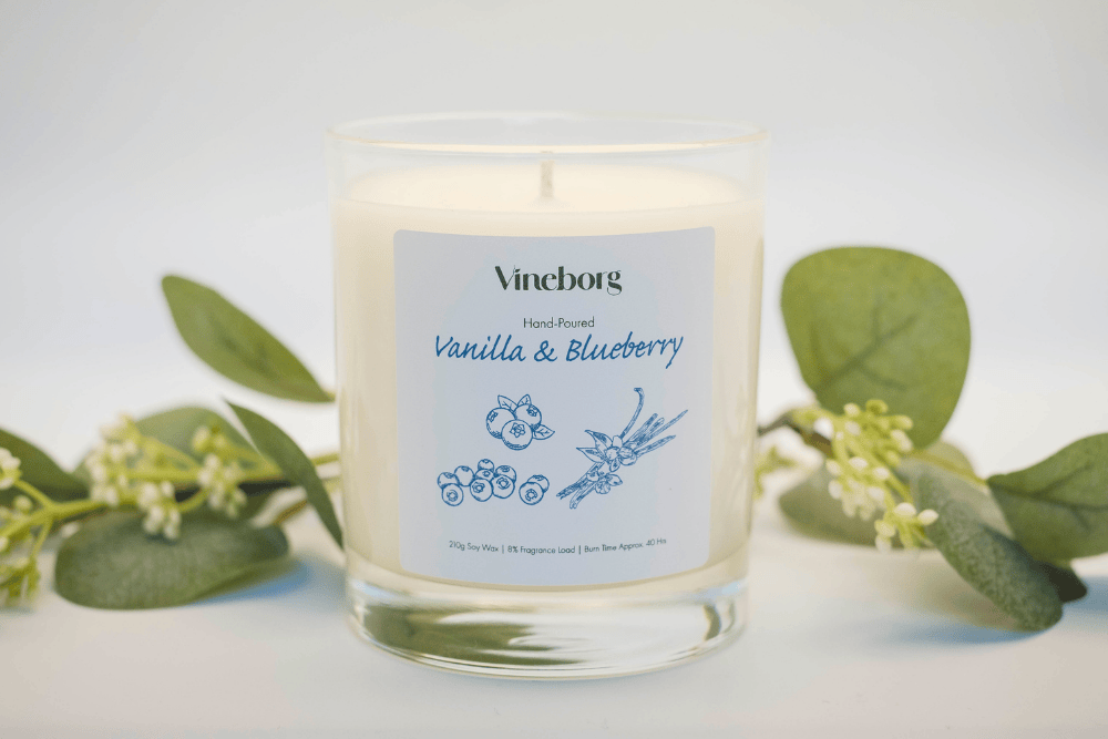 Vineborg vanilla and blueberry candle with green leaves on a light background