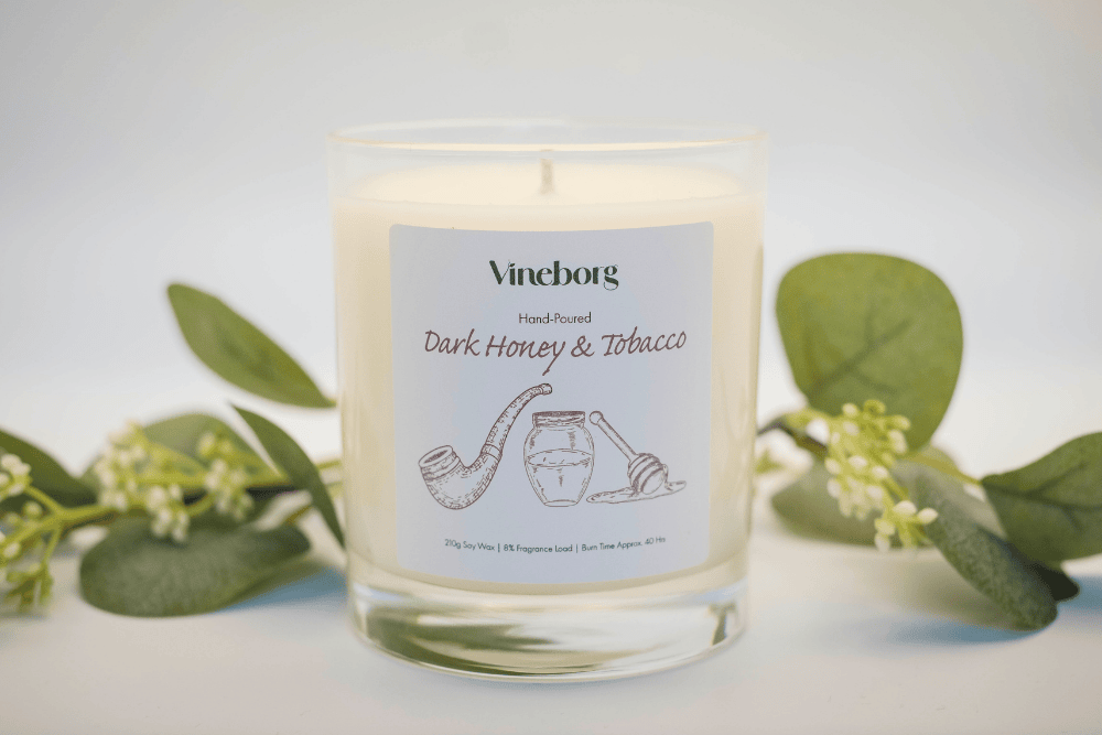 Vineborg candle labelled 'Dark Honey & Tobacco' with green leaves in the background